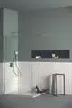 Duschbereich mit transparenter Glasabtrennung, braunem Boden und grauen Wänden. An der Wand ist eine Dusche von Ideal Standard montiert. Auf dem Boden stehen Pflegeprodukte.